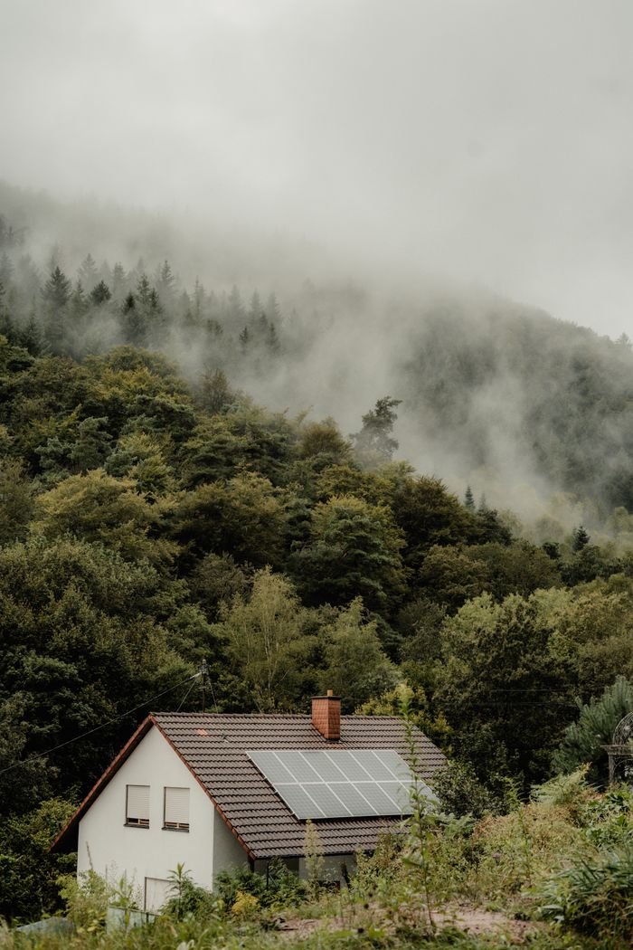 Services A house with solar panels nestled in a foggy forest, offering a serene and eco-friendly setting.