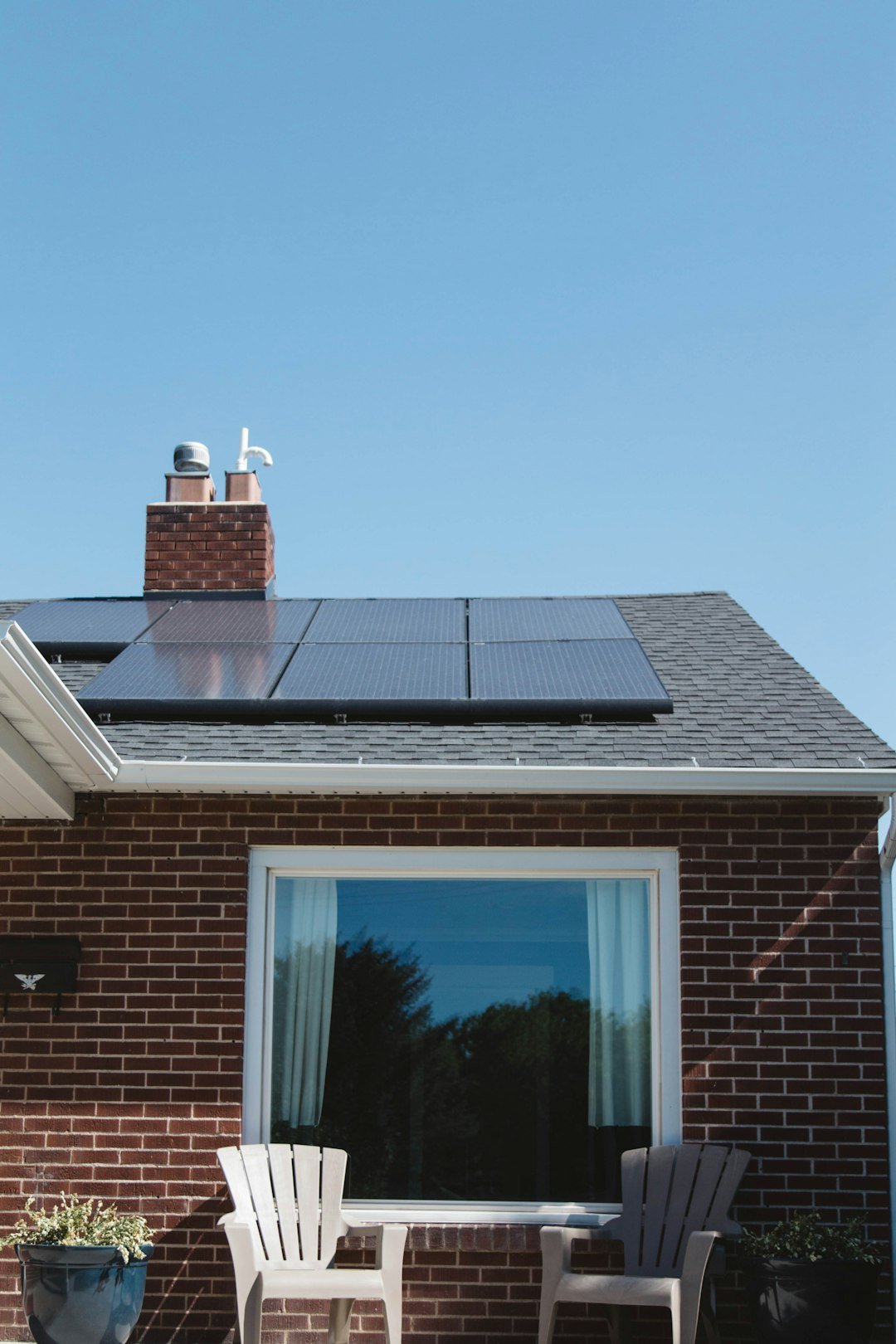 Services Vivint Solar - Solar Panels on roof of brick home with window and Adirondack chairs.