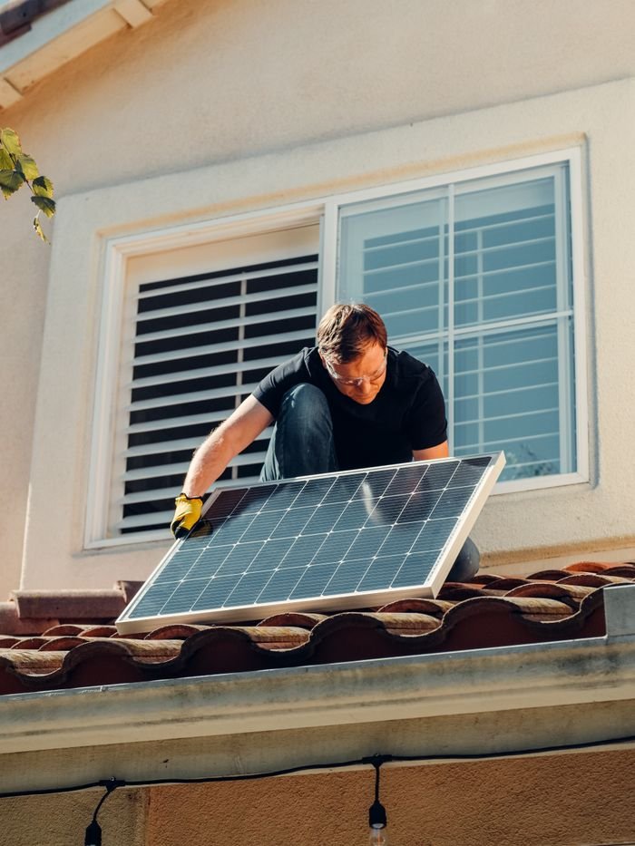 Services A worker installing a solar panel on a residential rooftop under bright sunlight.