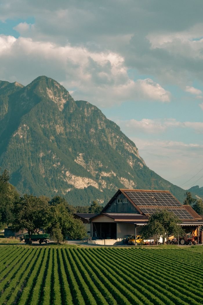Services Captivating view of a solar-powered barn amidst lush Swiss fields and alpine mountains.